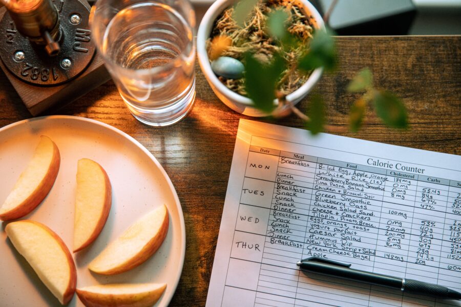 Paper with a meal plan and calories on it next to a plate with a sliced apple on it