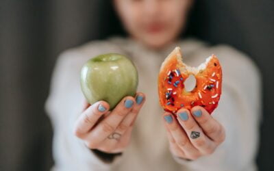 Person holding a bitten donut in one hand and a green apple in the other to represent ways to overcome food cravings in addiction recovery