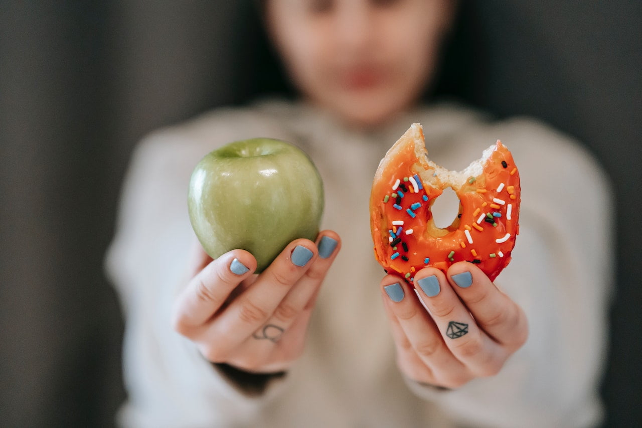 Person holding a bitten donut in one hand and a green apple in the other to represent ways to overcome food cravings in addiction recovery